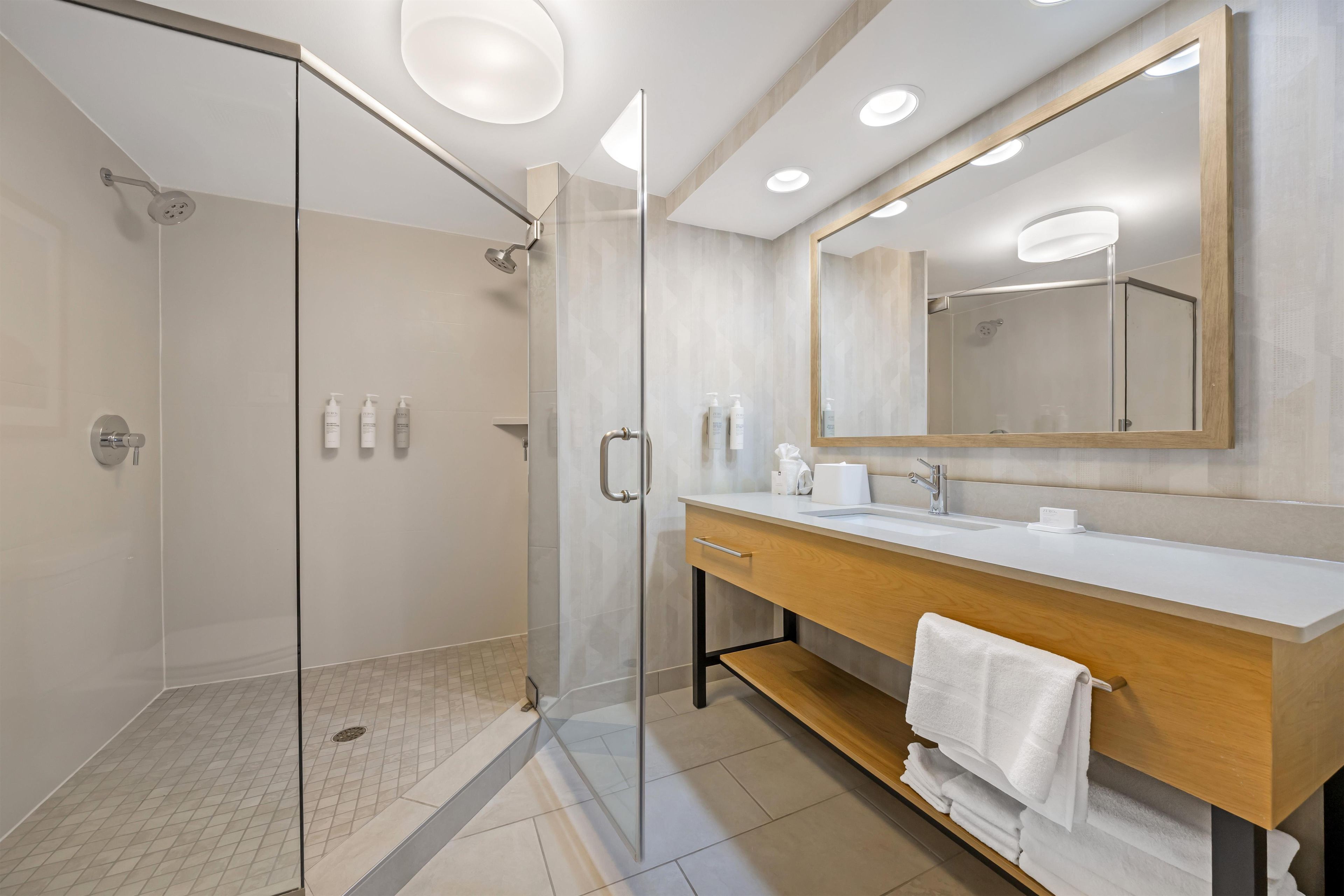 A modern bathroom with a glass shower enclosure, a wooden vanity with a mirror, and a tiled floor.