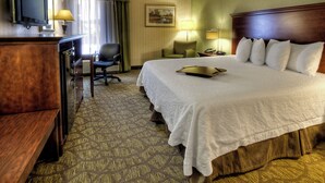 A hotel room with a large bed, a desk with a television, a chair, and a lamp.