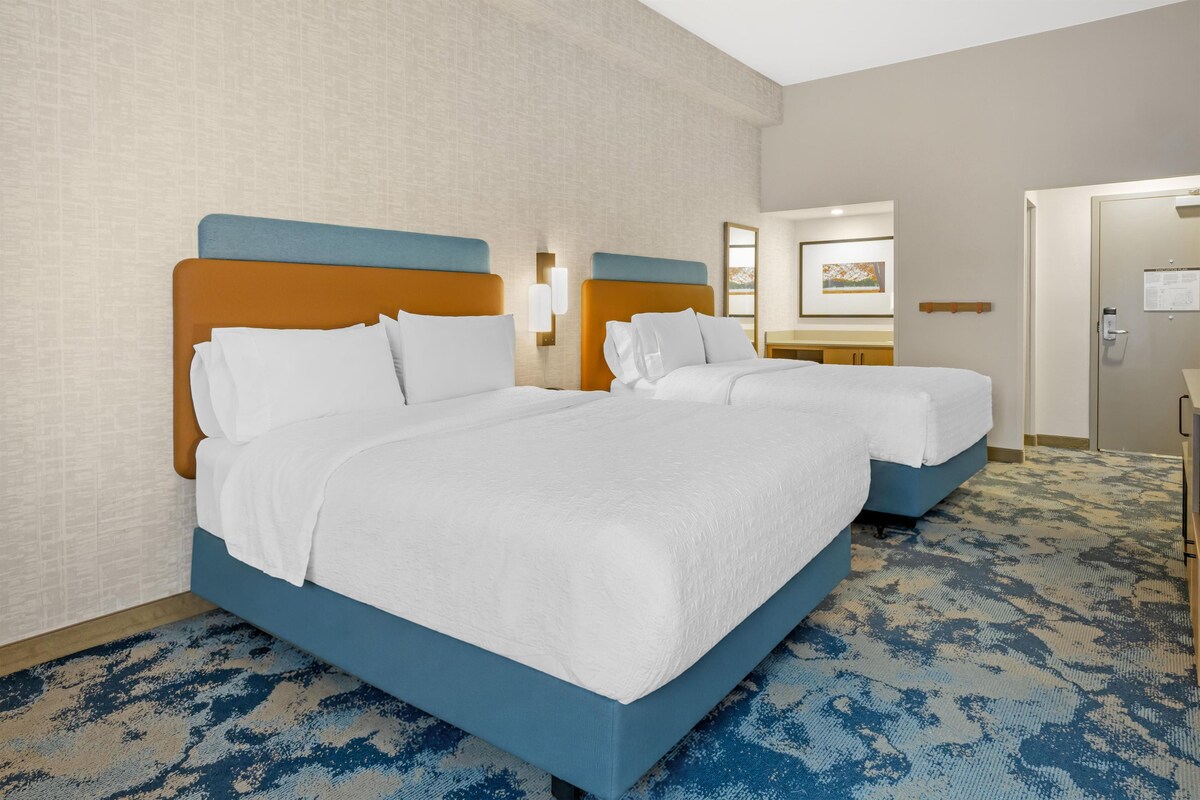 A hotel room with two beds, a large mirror, and a carpeted floor.