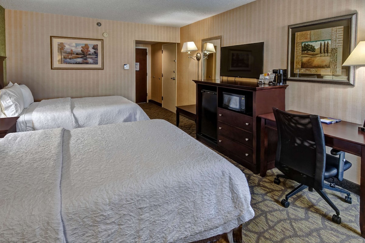 Een hotelkamer met twee bedden, een bureau, een stoel, een televisietoestel en een magnetron.