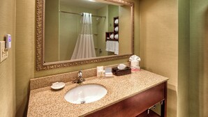 A bathroom with a large mirror, a sink, a towel rack, and a shelf with toiletries.