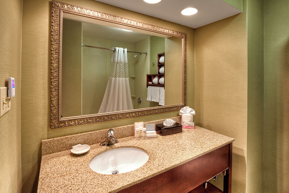 A bathroom with a large mirror, a sink, a towel rack, and a shelf with toiletries.