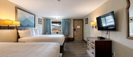 Habitación de hotel con dos camas, un televisor, un aparador y un cuadro de montañas.