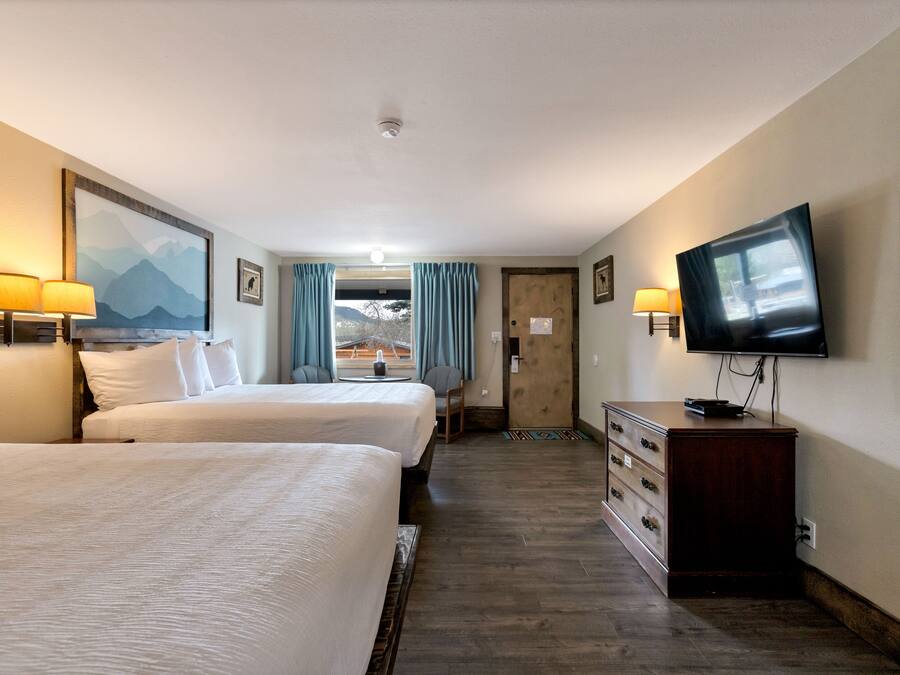 A hotel room with two beds, a TV, a dresser, and a painting of mountains.
