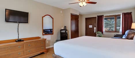 A bedroom with a large bed, wooden dresser, ceiling fan, TV, and a window with curtains.