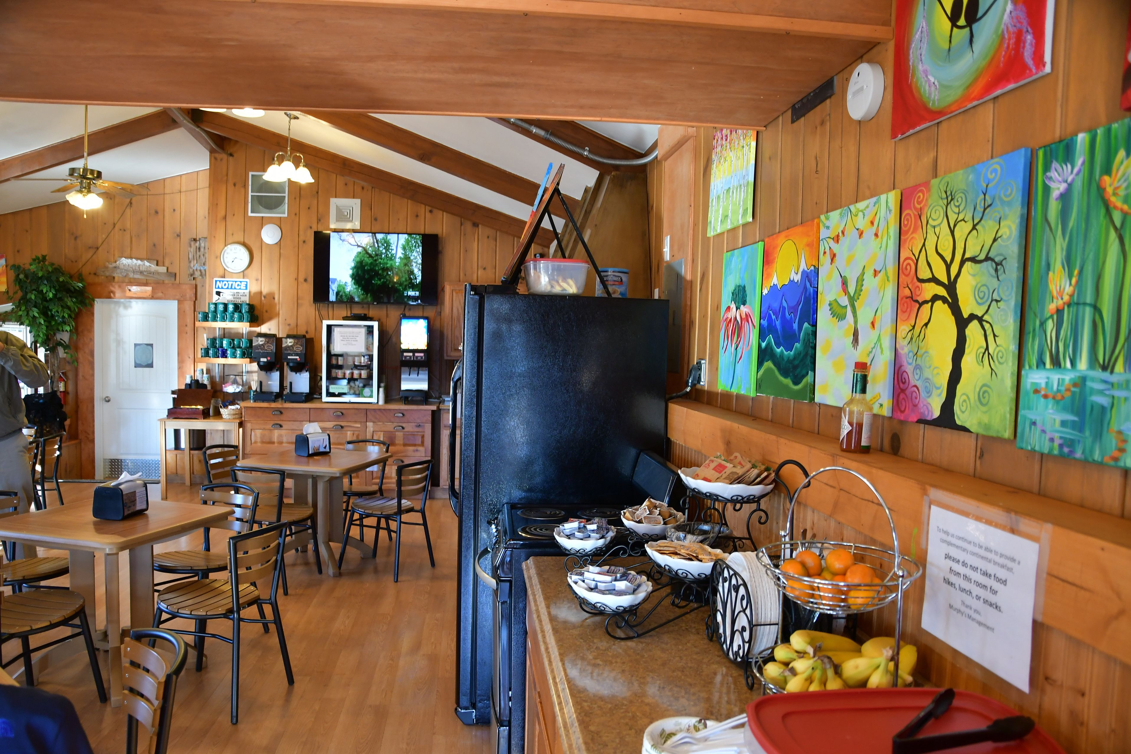 Una cucina rustica con pareti in legno, una stufa nera e vari utensili da cucina. Sono presenti dipinti colorati alle pareti e un cartello che indica il divieto di consumare cibo all'interno.