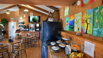 Una cucina rustica con pareti in legno, una stufa nera e vari utensili da cucina. Sono presenti dipinti colorati alle pareti e un cartello che indica il divieto di consumare cibo all'interno.