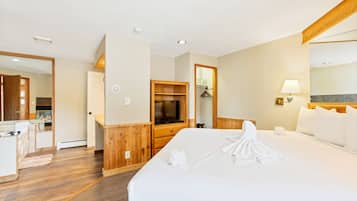 Habitación de hotel con una cama grande, paneles de madera, televisor, espejo y una pequeña kitchenette.