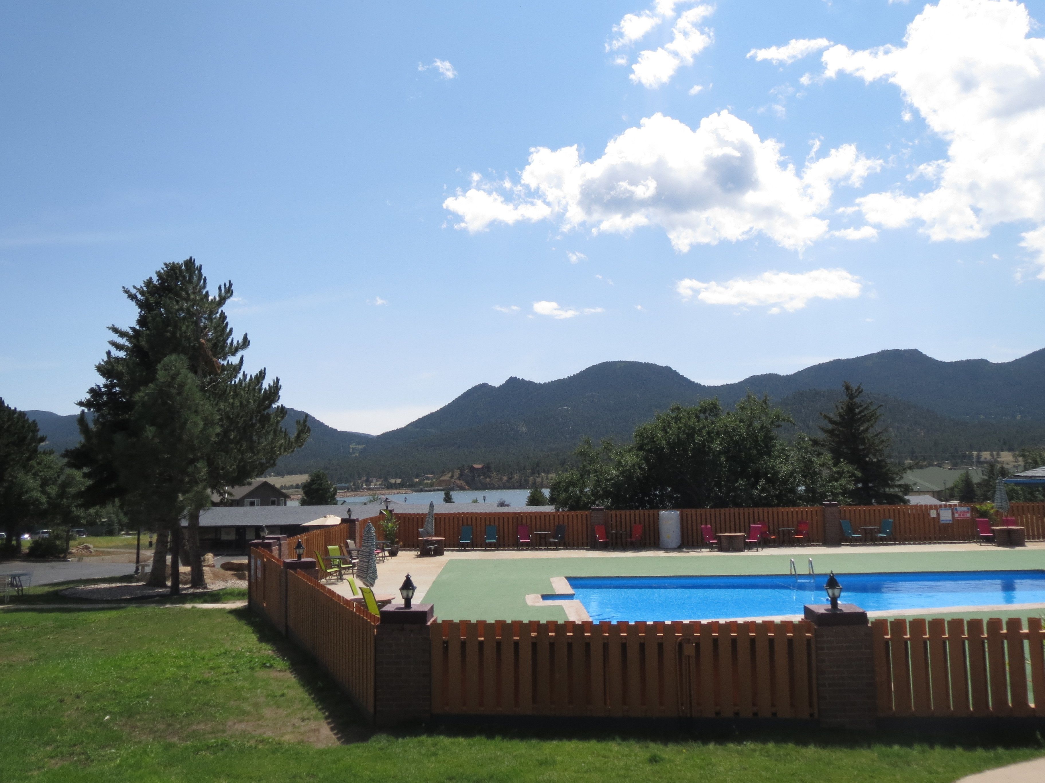 Una piscina con cerramiento de madera, rodeada de césped y árboles, con montañas al fondo.