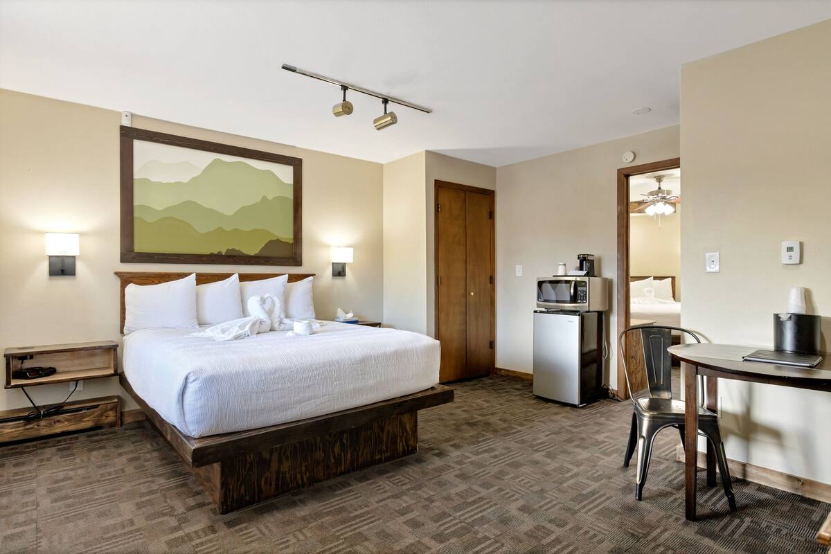 A hotel room with a large bed, a desk with a chair, a microwave, and a refrigerator.