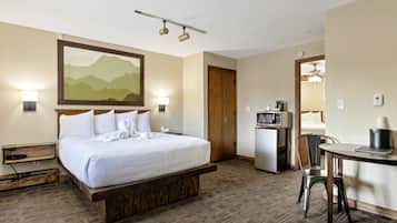 A hotel room with a large bed, a desk with a chair, a microwave, and a refrigerator.