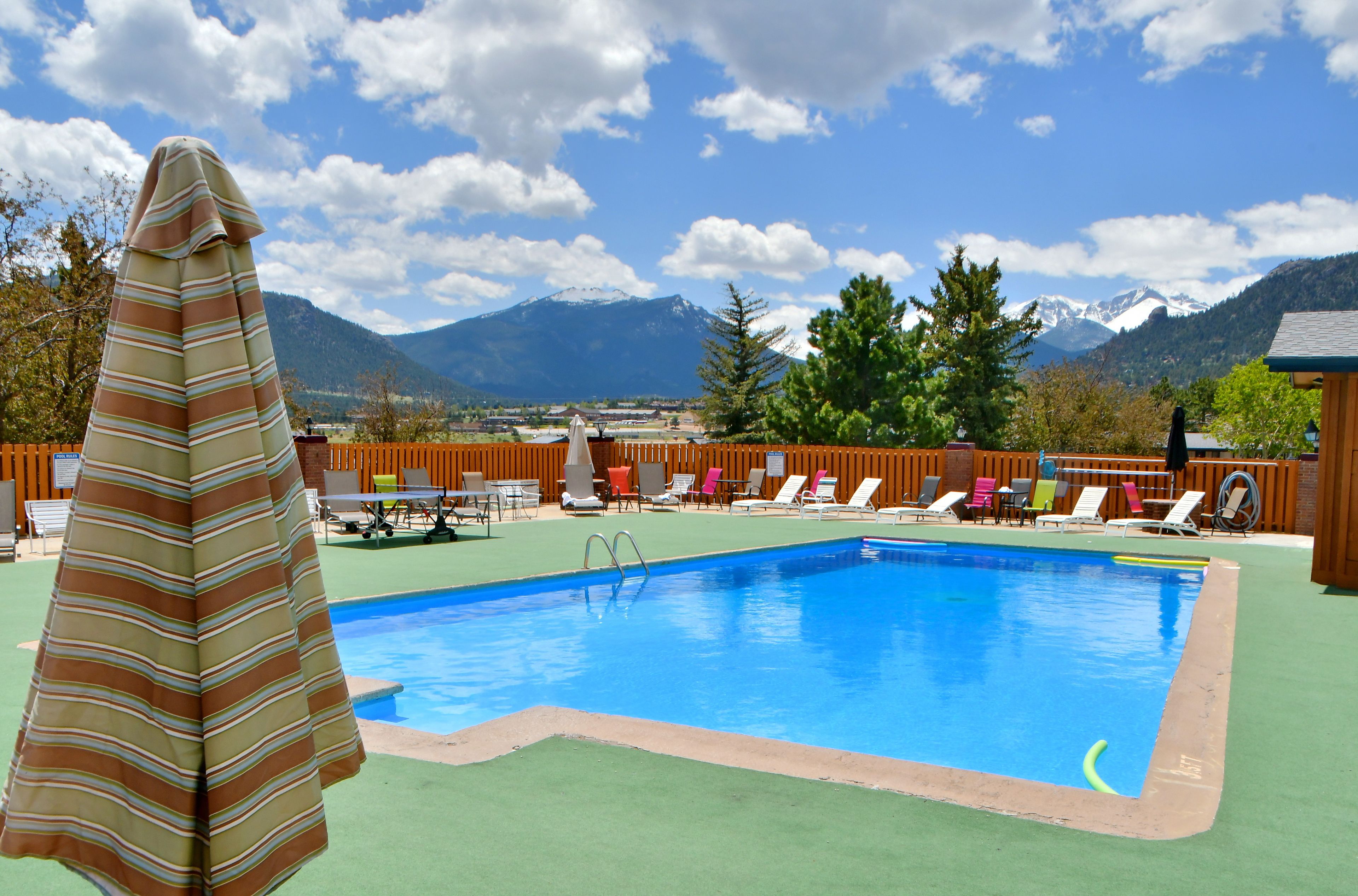 Une piscine entourée de montagnes et d’arbres, avec des chaises longues et un parasol rayé.