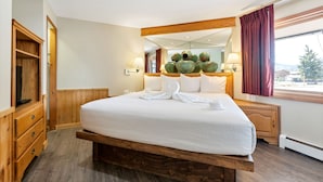 Une chambre d’hôtel avec un grand lit, une tête de lit en bois, une armoire en bois, un miroir au-dessus du lit et une fenêtre avec des rideaux.