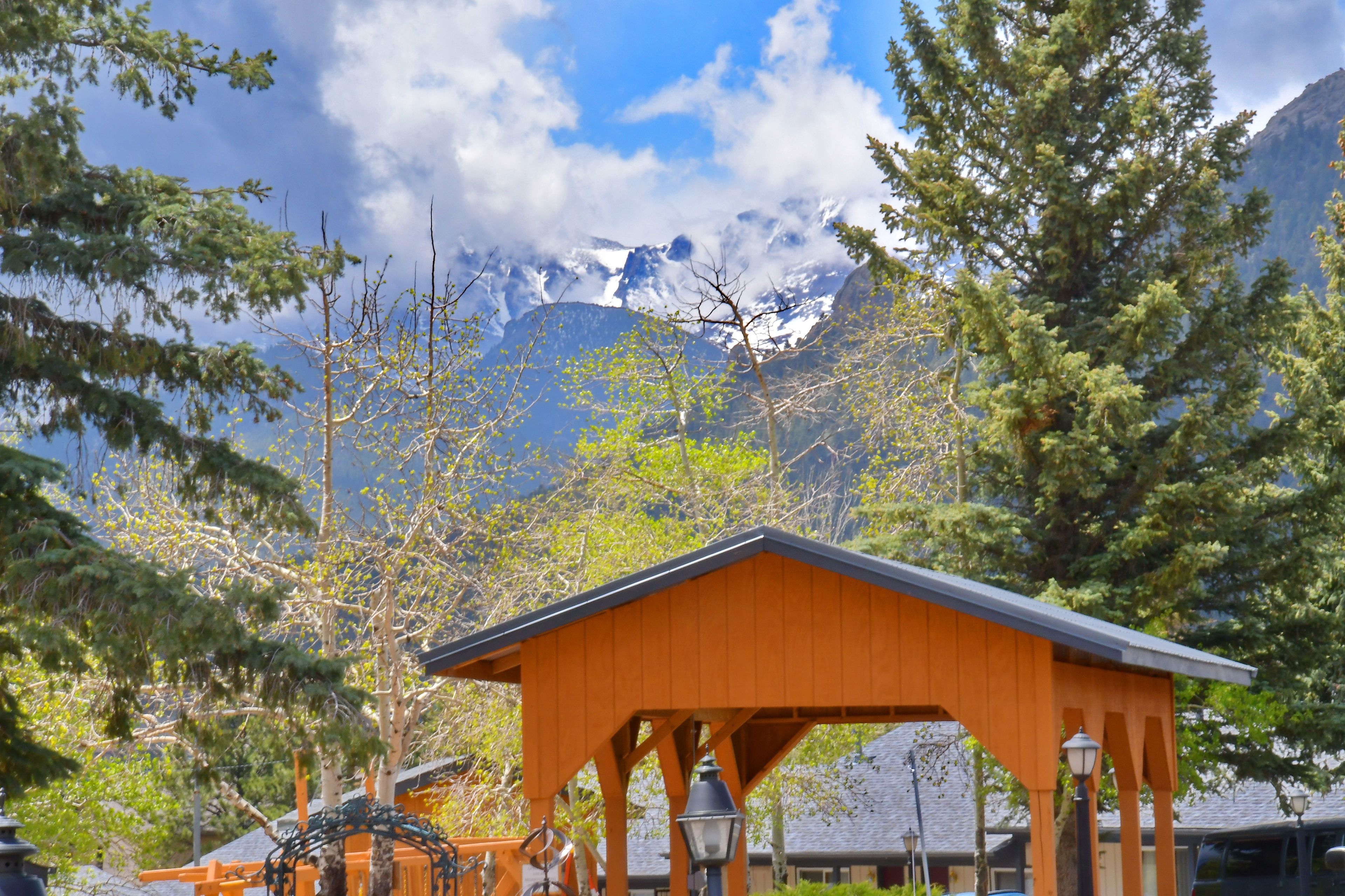 Un pavillon en bois doté d’un toit en pente, entouré d’arbres et avec une chaîne de montagnes en arrière-plan.