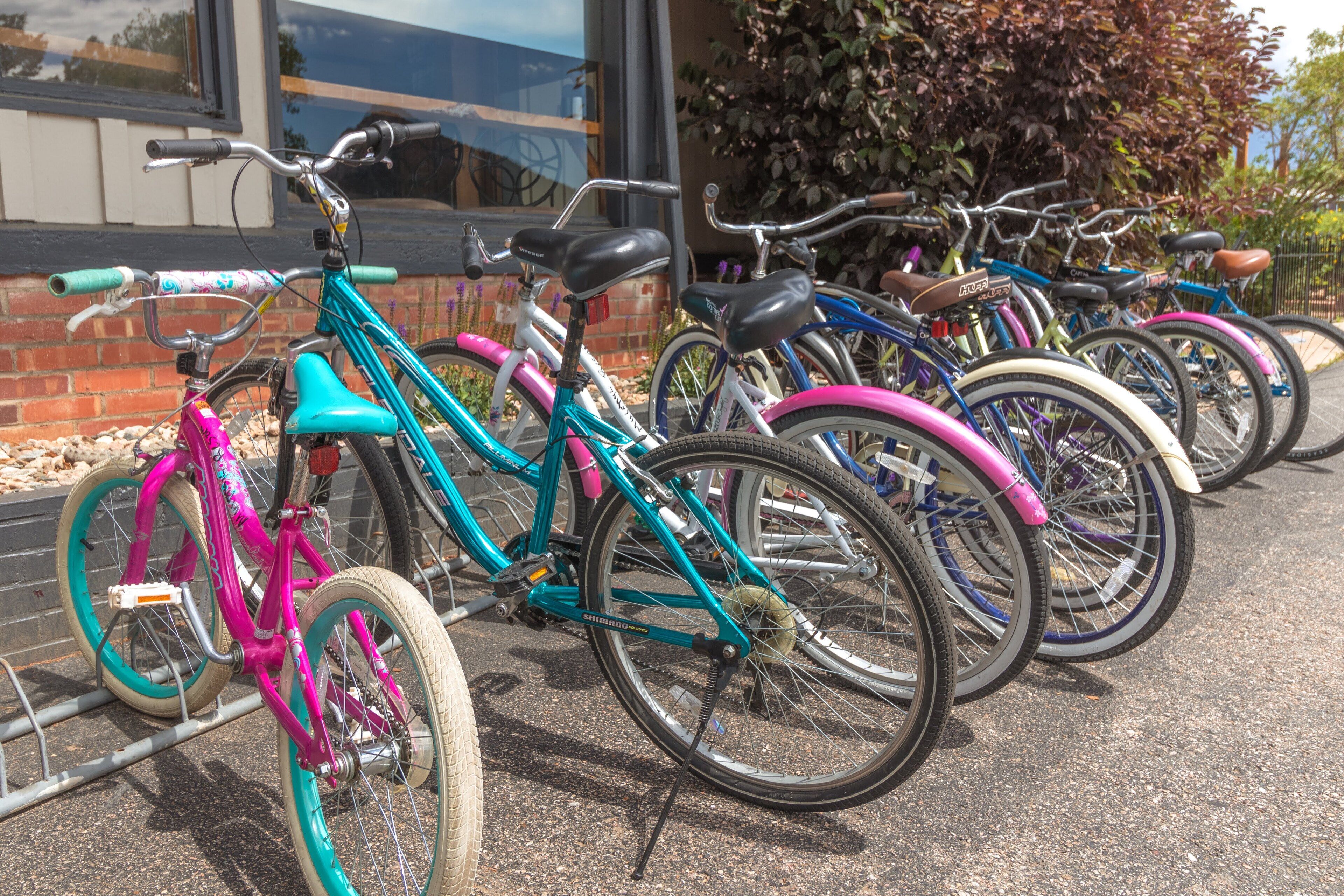 Une rangée de vélos est garée devant un immeuble à la façade en briques et doté d’une grande fenêtre.