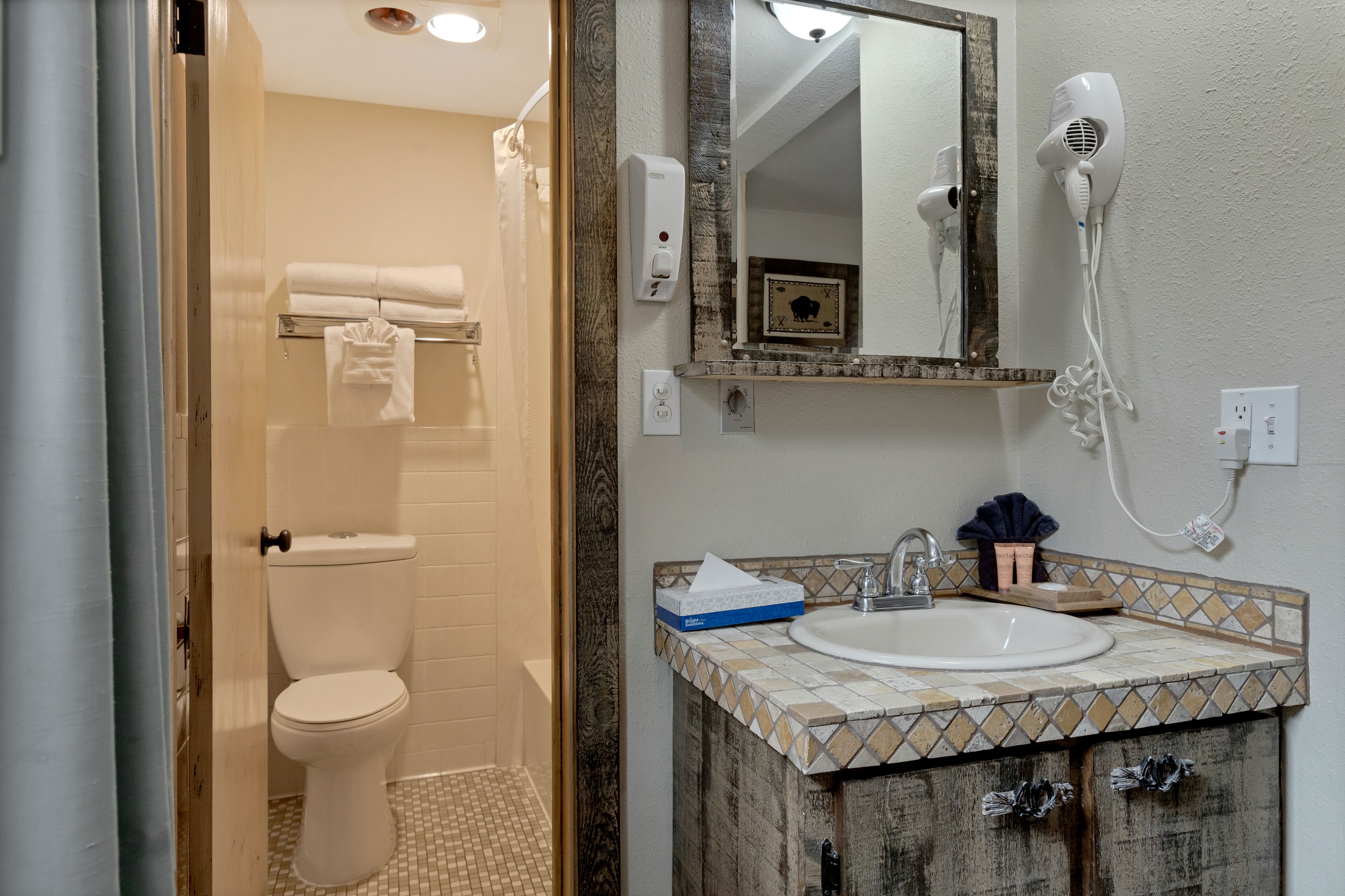 Une salle de bain comprenant des toilettes, un lavabo, un miroir, un sèche-cheveux et un porte-serviettes.