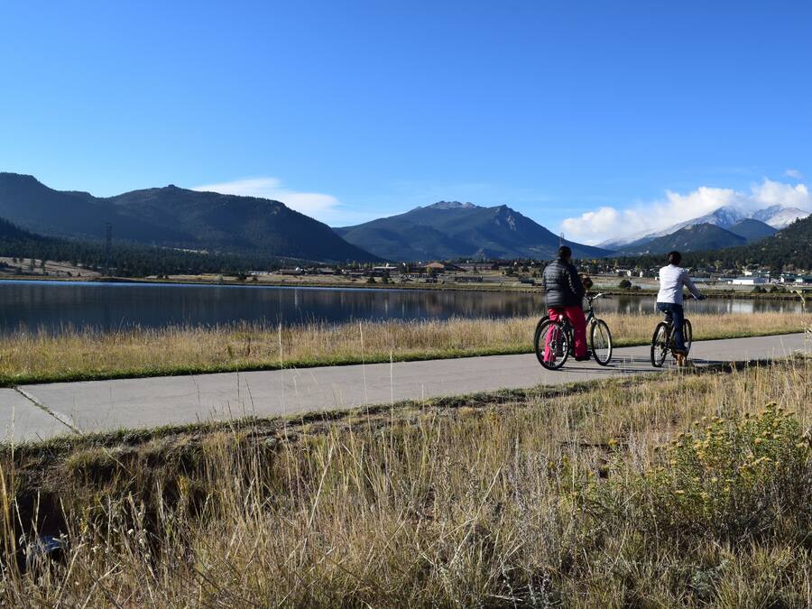 Un sendero pavimentado junto a un lago, con montañas al fondo.