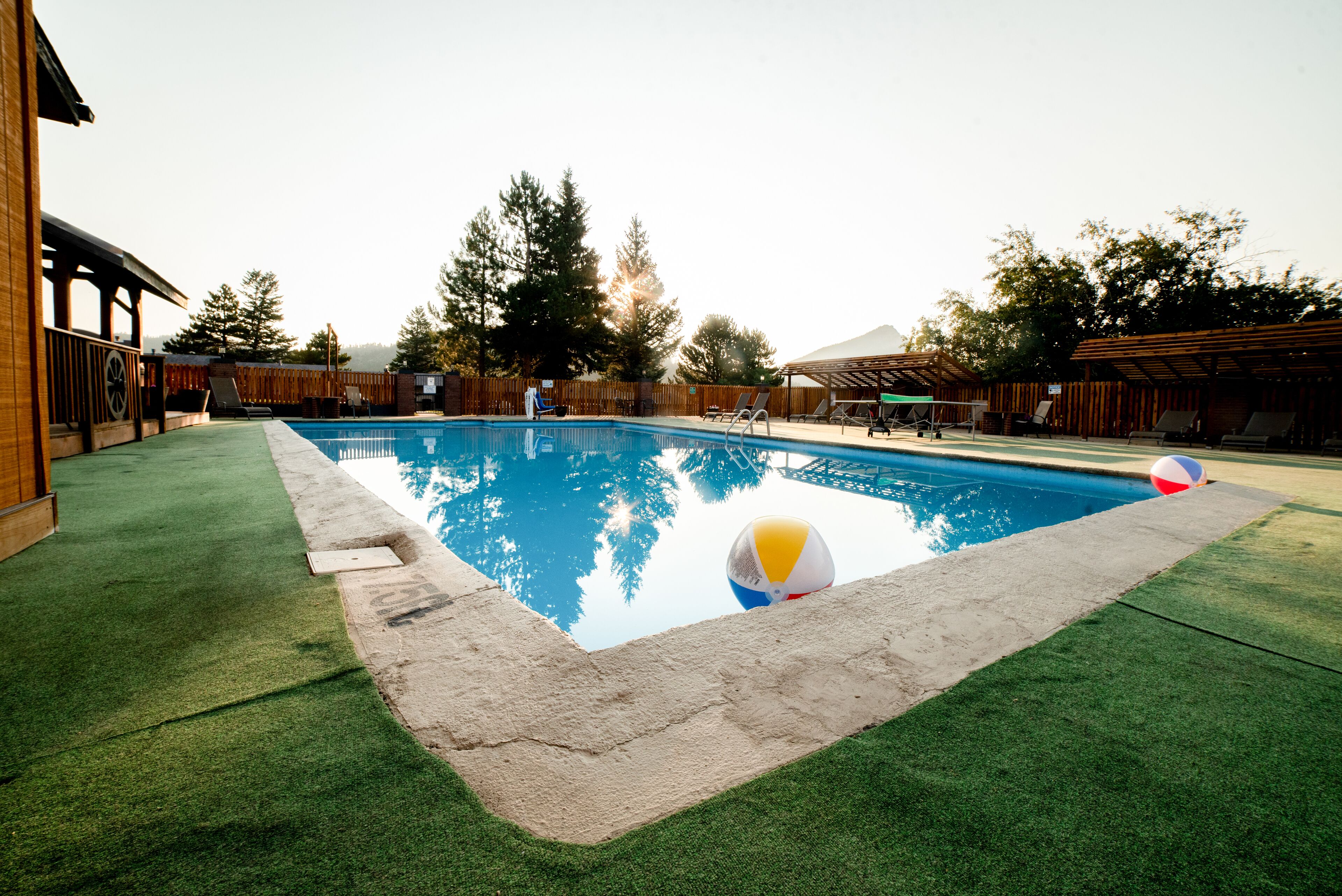 Una piscina con césped artificial, una terraza de madera y una pelota de playa.