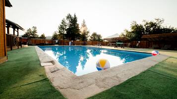Una piscina con césped artificial, una terraza de madera y una pelota de playa.