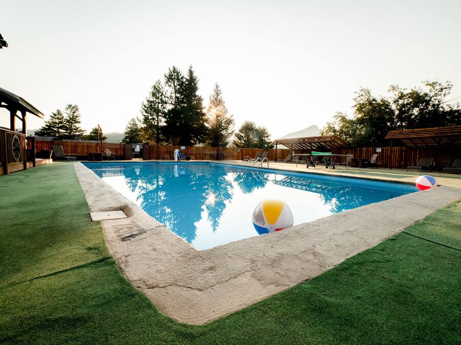 Una piscina con césped artificial, una terraza de madera y una pelota de playa.