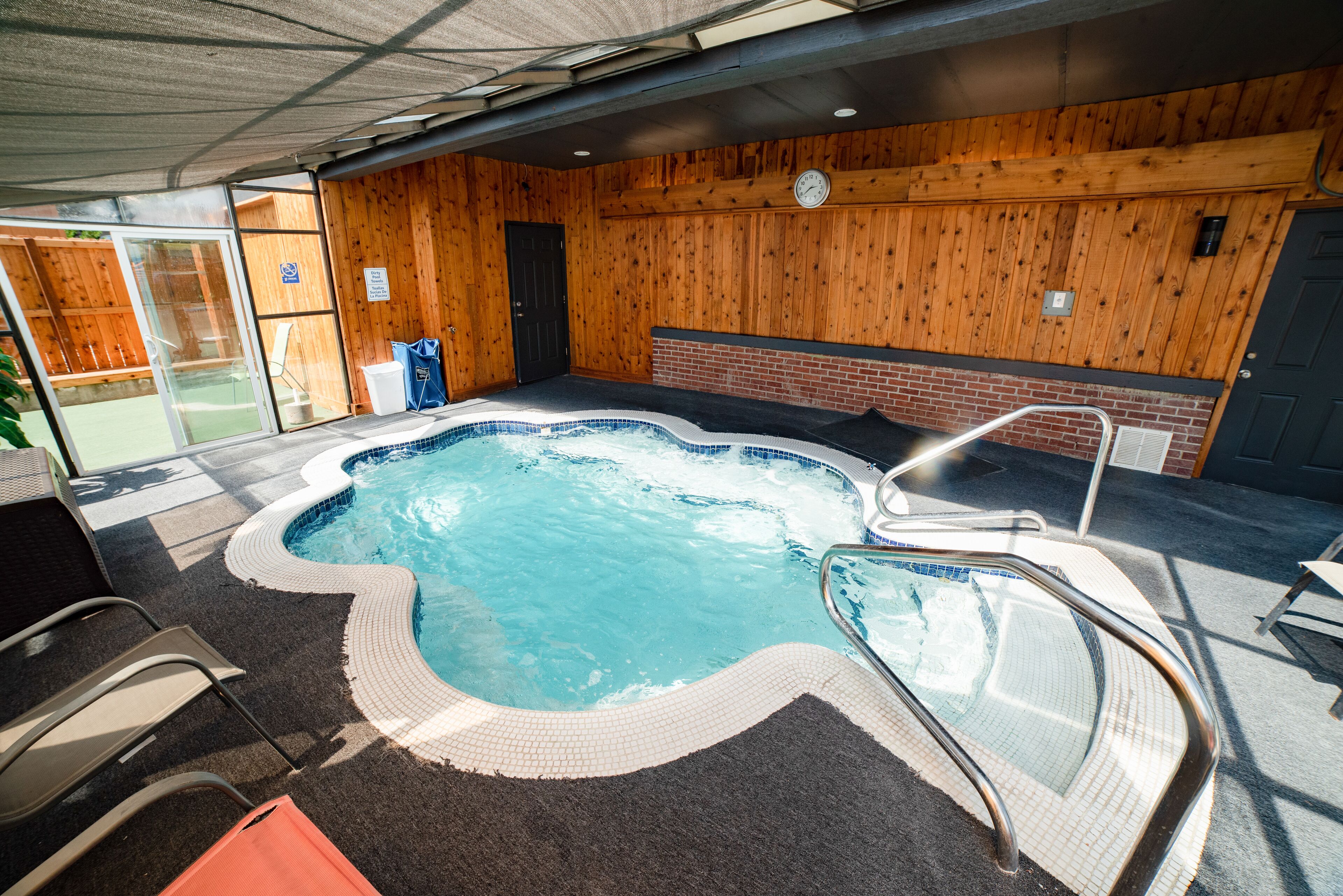 Un jacuzzi con borde de azulejos, una escalera metálica y una pared de madera con un reloj.