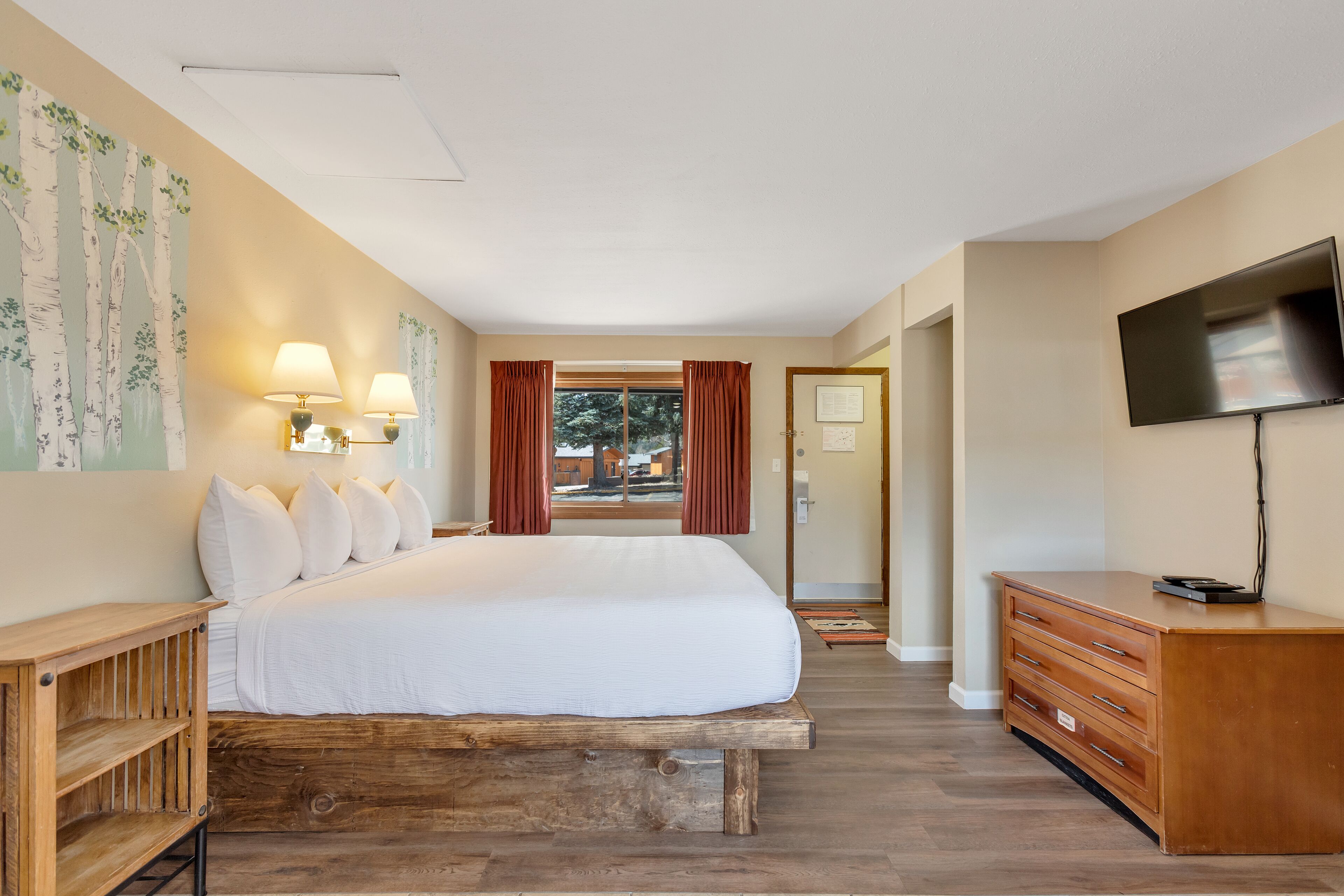 A bedroom with a large bed, wooden headboard, bedside lamps, a TV, and a dresser.