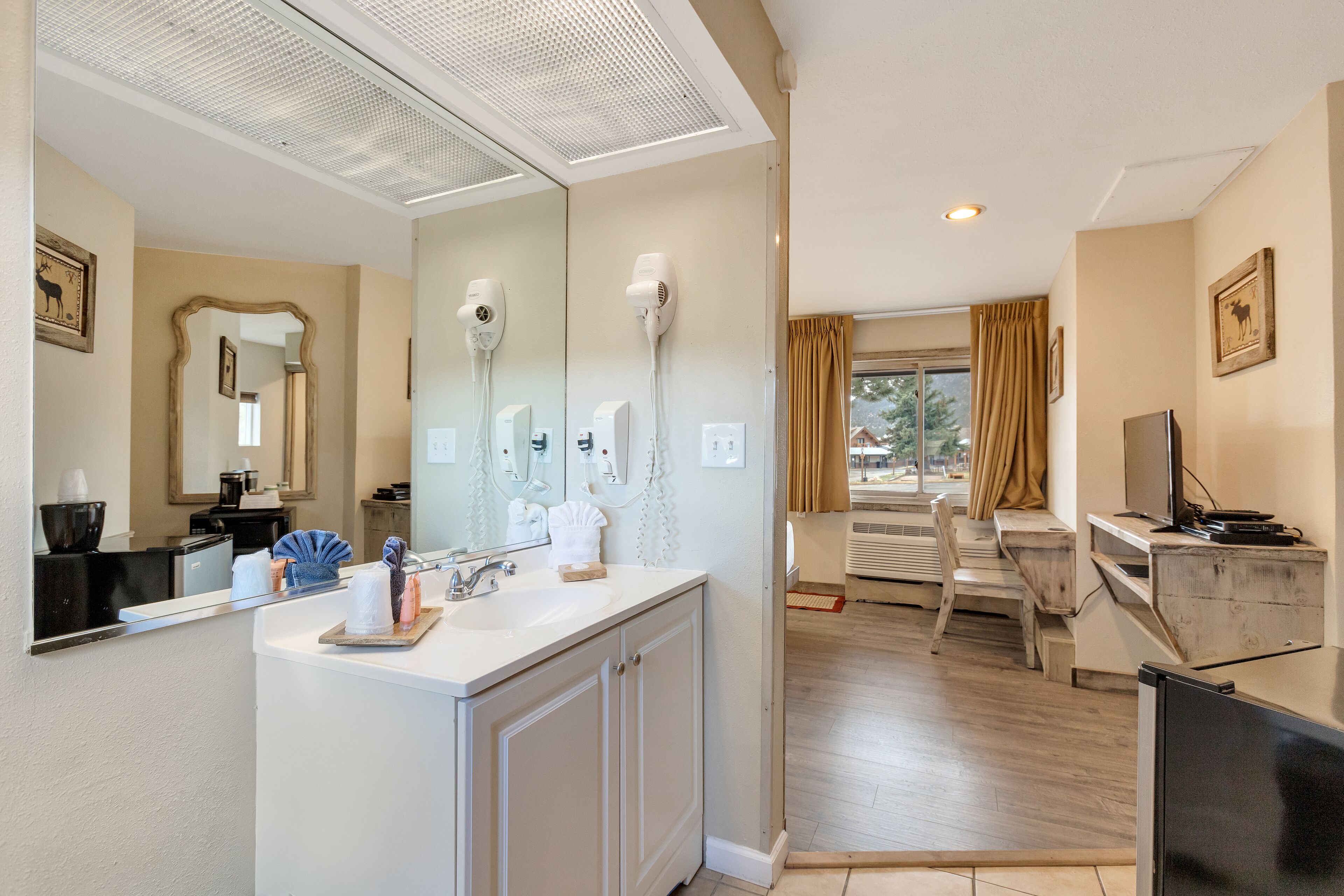 A modern bathroom with a large mirror, two hair dryers, a sink, and a vanity.