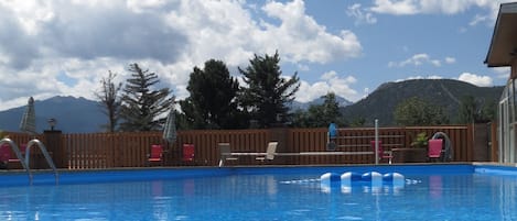 A swimming pool with a wooden fence, chairs, and a mountain view in the background.
