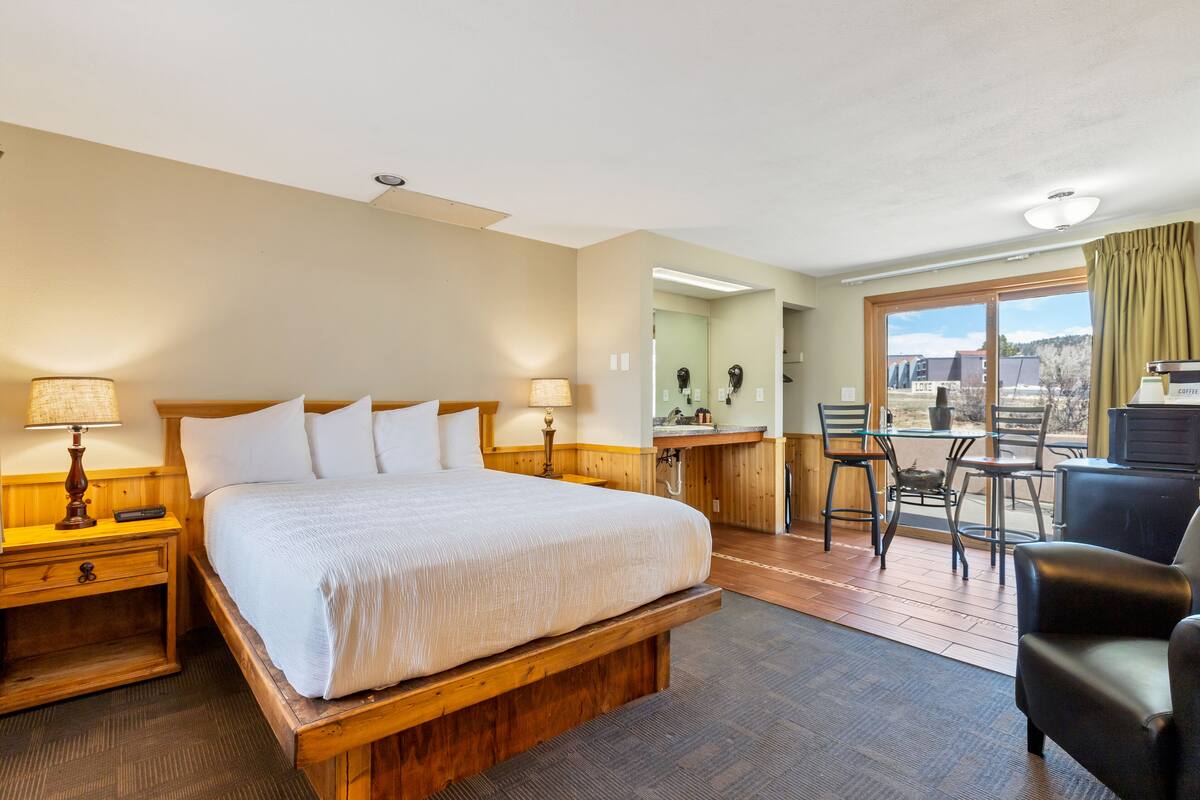 A hotel room with a large bed, a desk with a chair, a coffee machine, and a view of the outdoors.