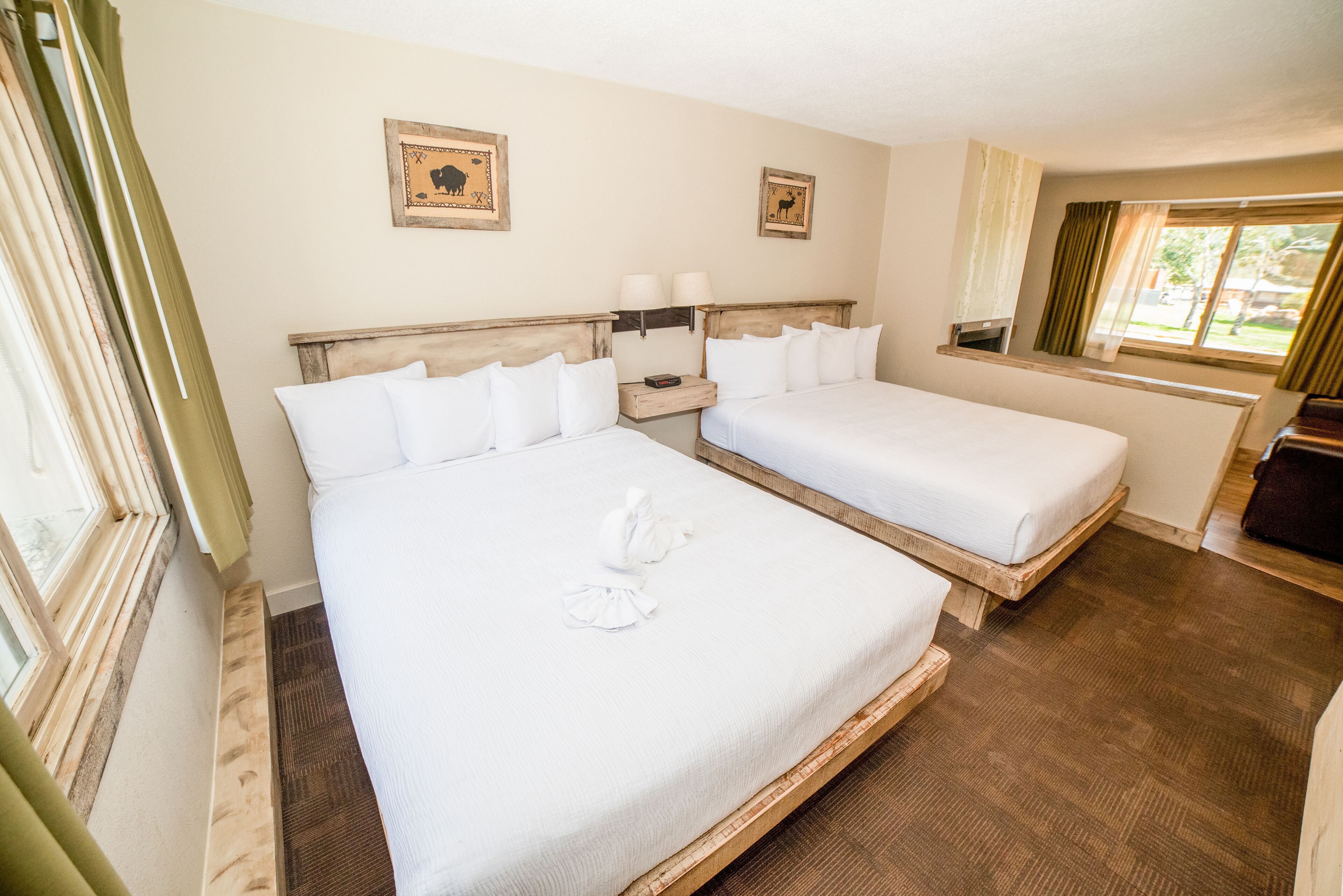 Habitación de hotel con dos camas, cabecera de madera, mesitas de noche con lámparas y una ventana con cortinas.