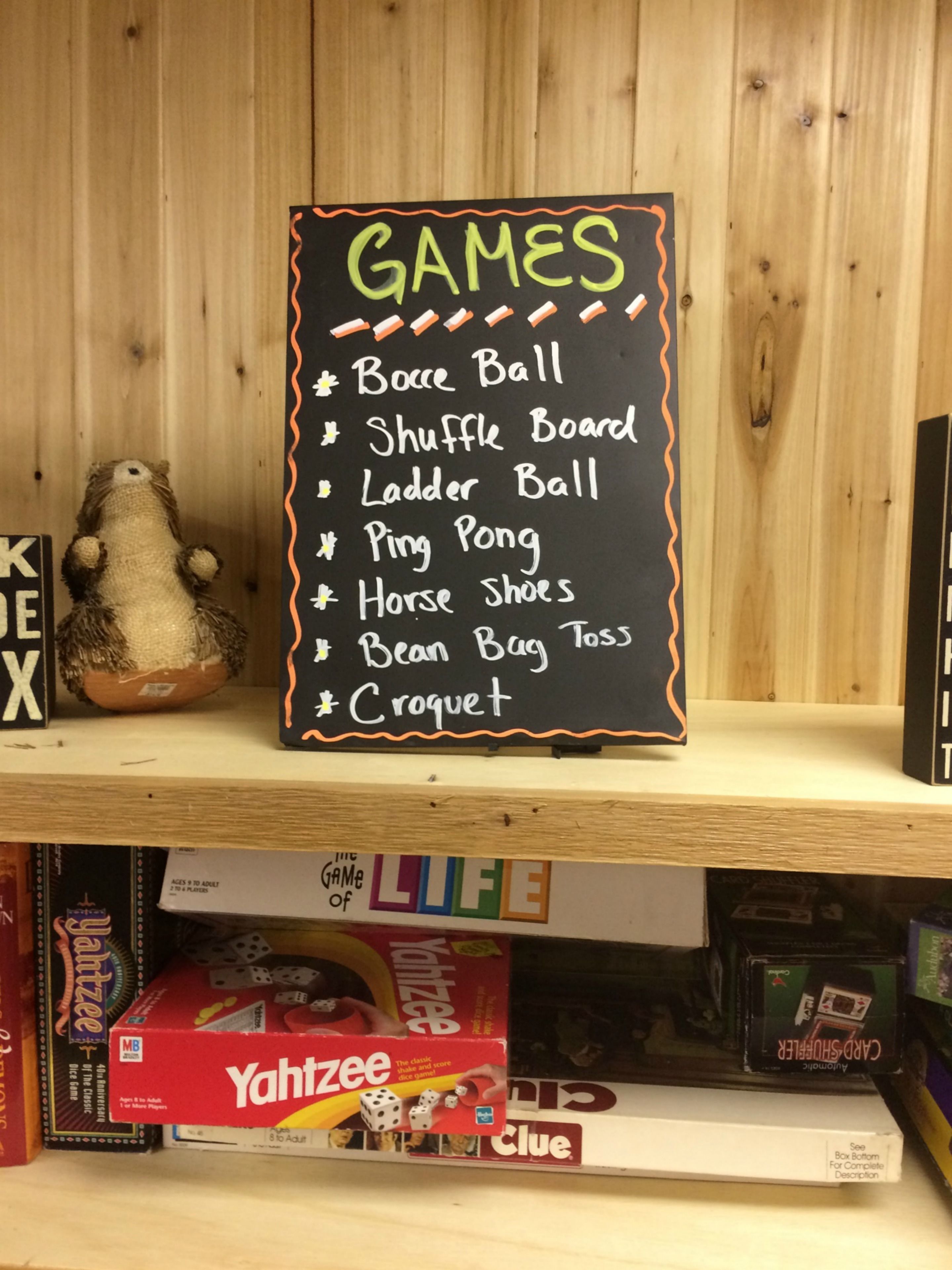 A shelf with a chalkboard listing various games like Bouncy Ball, Shuffle Board, and Croquet.