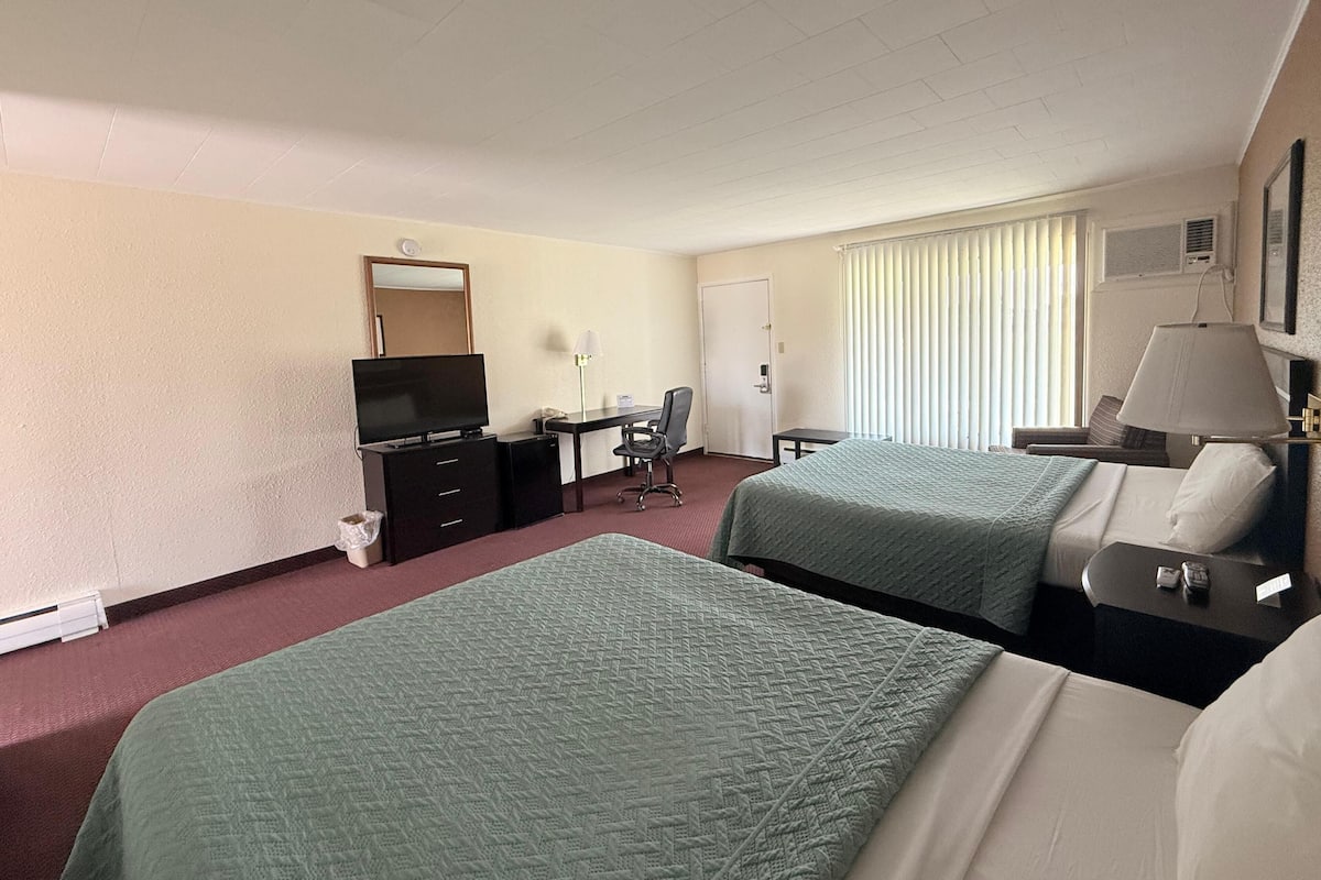 A hotel room with two beds, a desk with a chair, a television, a lamp, and a window with blinds.