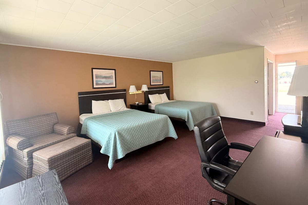 A hotel room with two beds, a sofa, a chair, a desk, and a lamp.