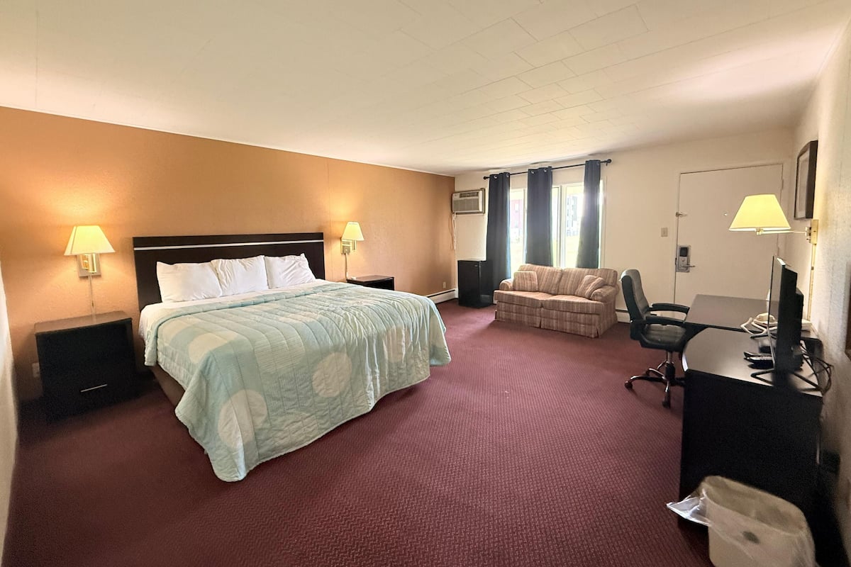 A hotel room with a bed, a desk, a chair, a sofa, and two lamps.