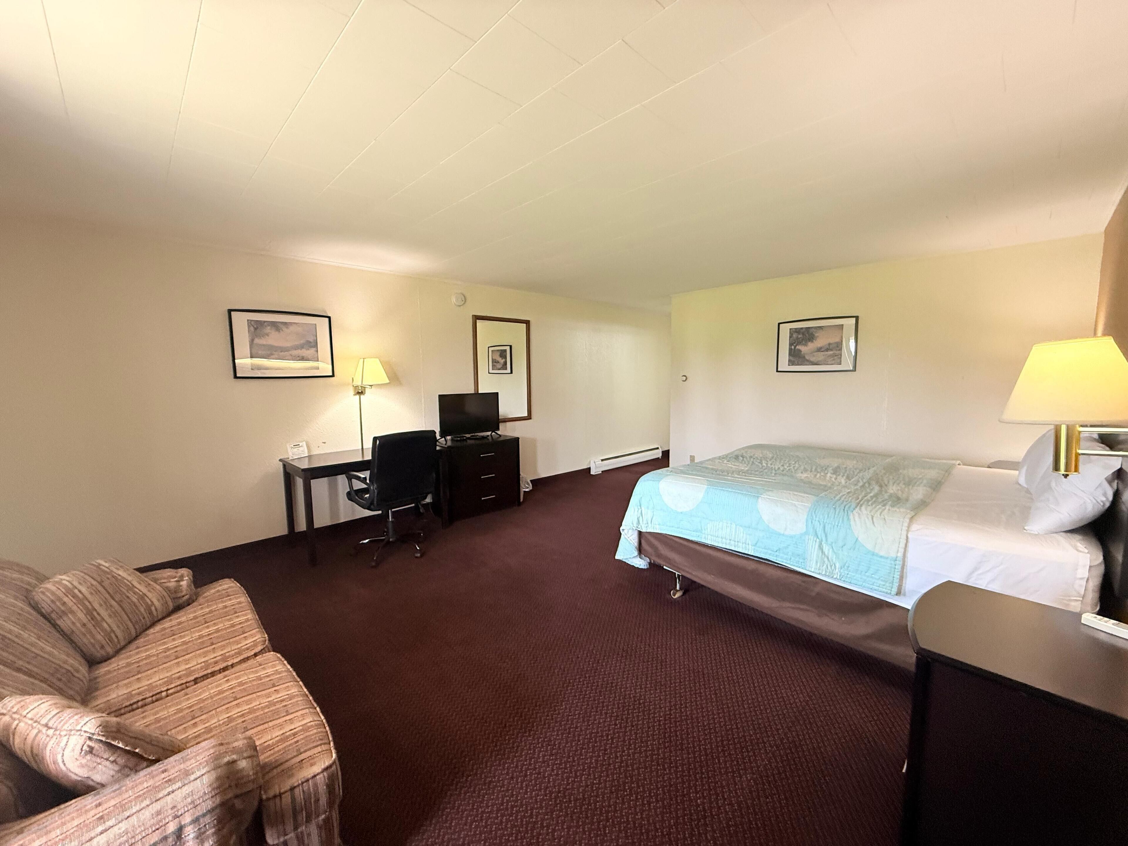 A hotel room with a bed, a desk with a chair, a couch, and two wall-mounted lamps.