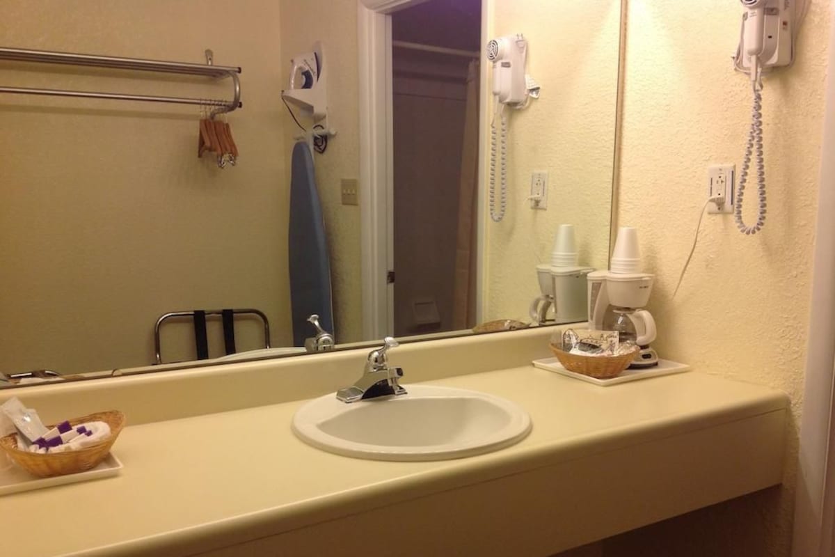 Une salle de bain d’hôtel équipée d’un lavabo, d’un miroir, d’un porte-serviettes et d’un sèche-cheveux.