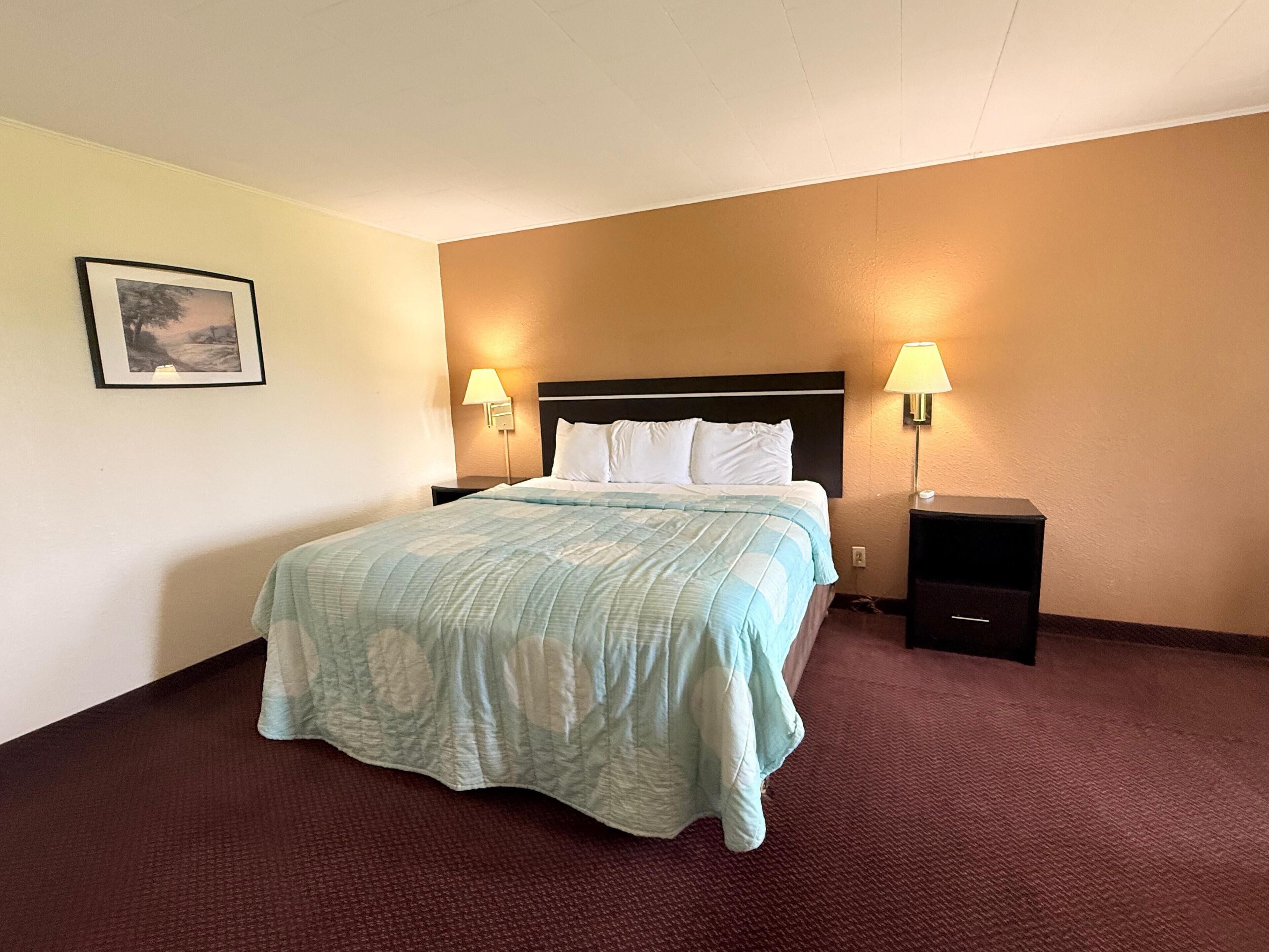 A hotel room with a bed, two bedside lamps, a nightstand, and a framed picture on the wall.