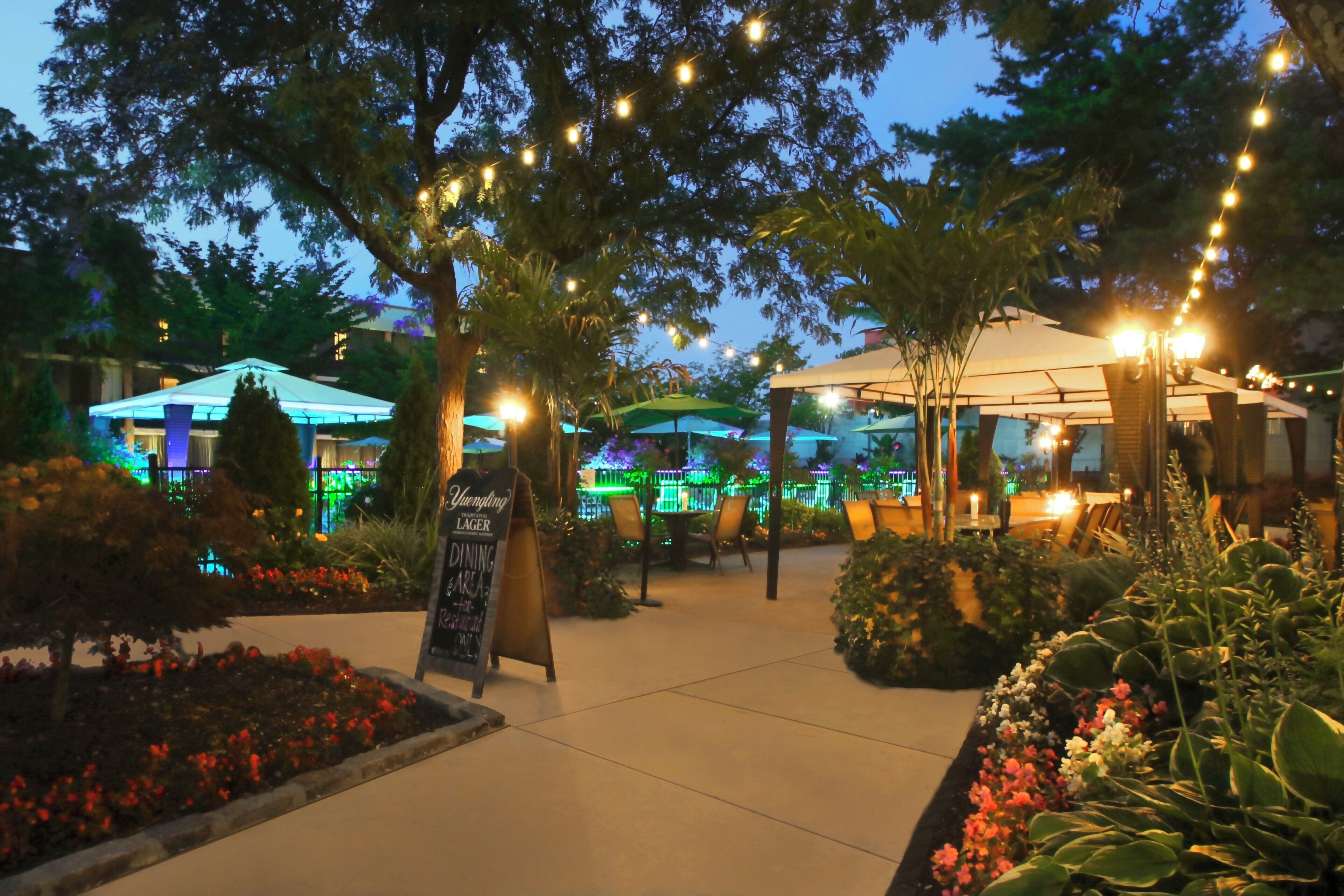 Un área de comedor al aire libre con luces colgantes, sombrillas y un letrero que anuncia cerveza Yuengling lager.