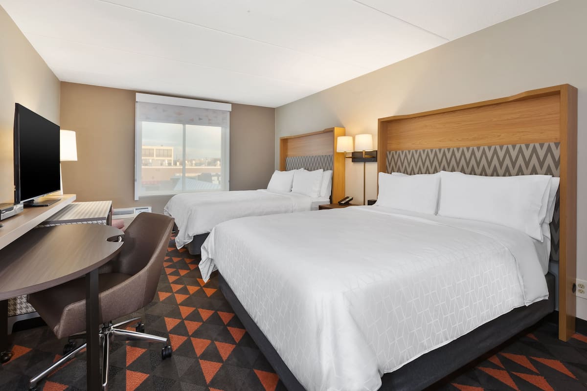 A hotel room with two beds, a desk with a computer, and a chair.