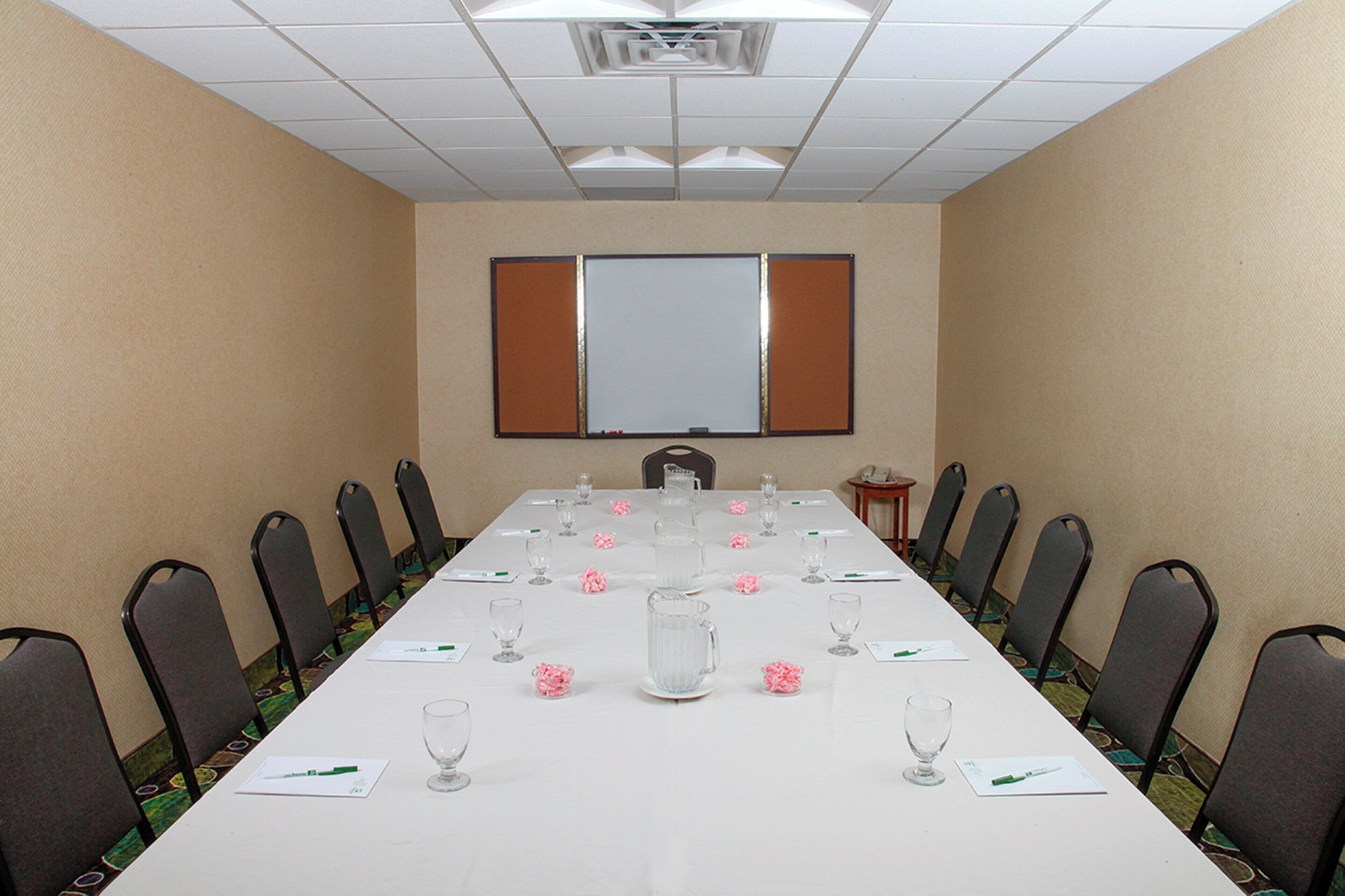 Un salón de conferencias con una larga mesa, sillas, una pantalla de proyector y una pizarra.