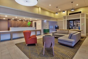 A modern hotel lobby with a reception desk, seating area, and a restaurant entrance. - Holiday Inn Westbury - Long Island by IHG (Carle Place)