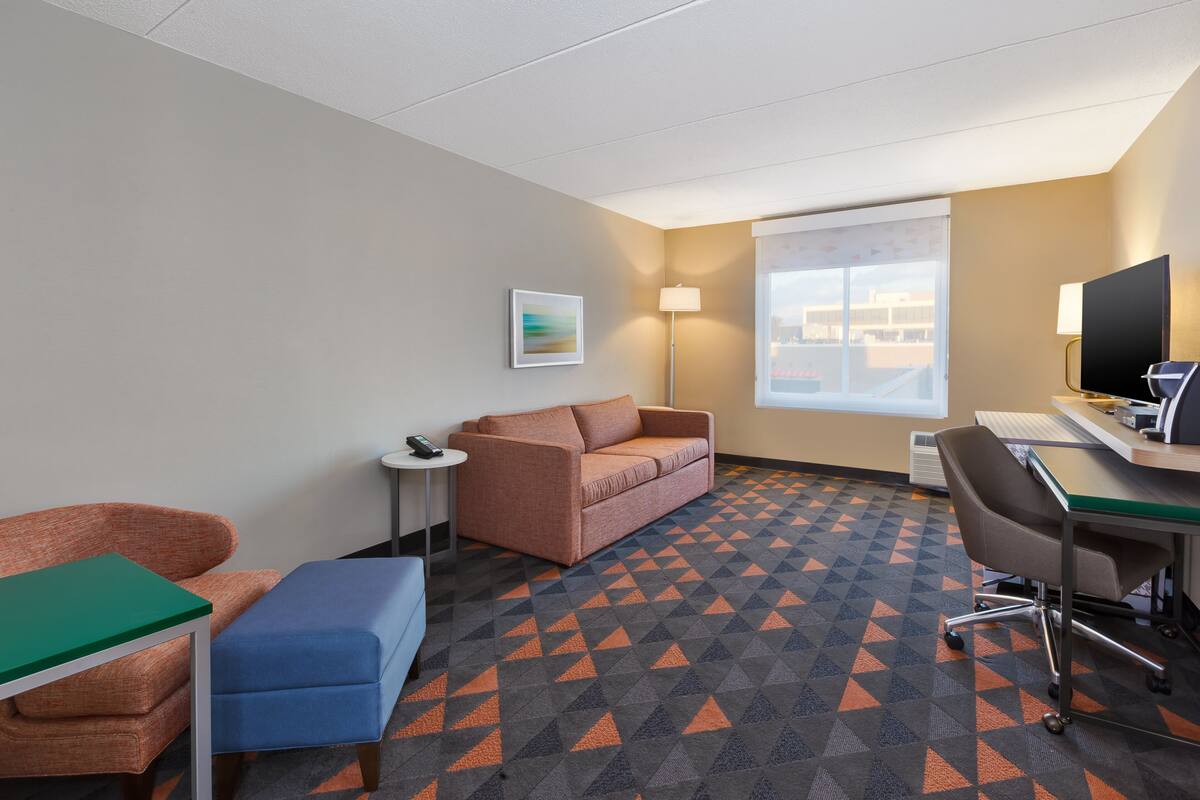 A hotel room with a sofa, a small table, a desk with a computer, and a patterned carpet.