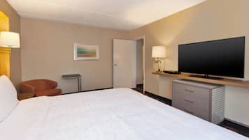 Ein Hotelzimmer mit einem großen Bett, einem Fernseher, einem Schreibtisch mit Lampe und einem Sessel.