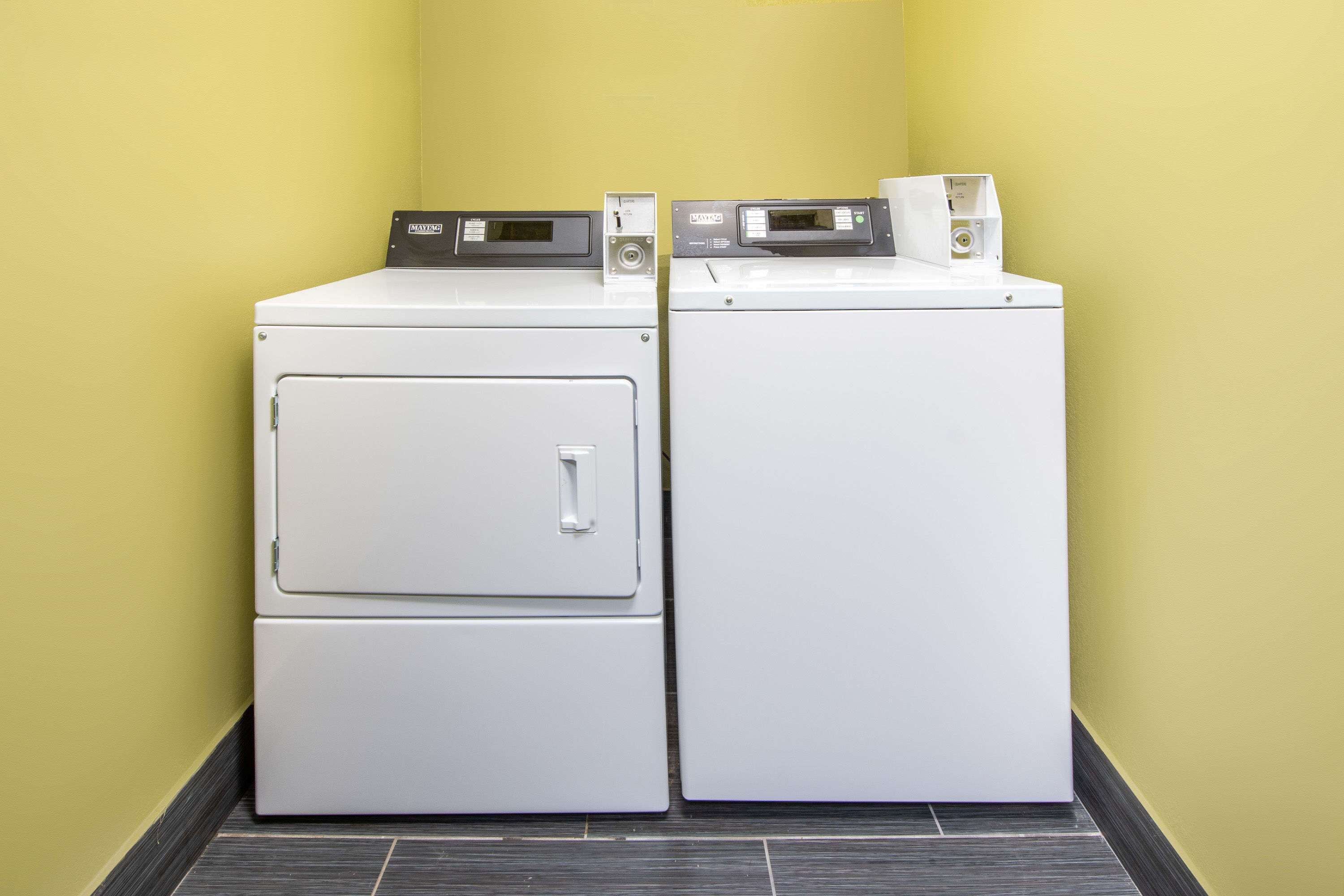 Two stacked white washing machines in a corner with a yellow wall and dark floor tiles.