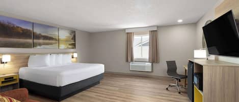 Ein Hotelzimmer mit einem großen Bett, einem Schreibtisch mit Computer, einem Fernseher und einem Fenster mit Vorhängen.
