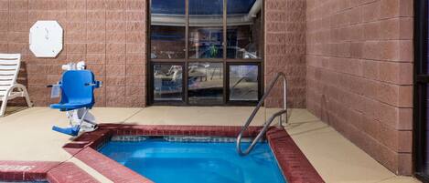 A small indoor pool with a blue water feature, a ladder, and a chair.