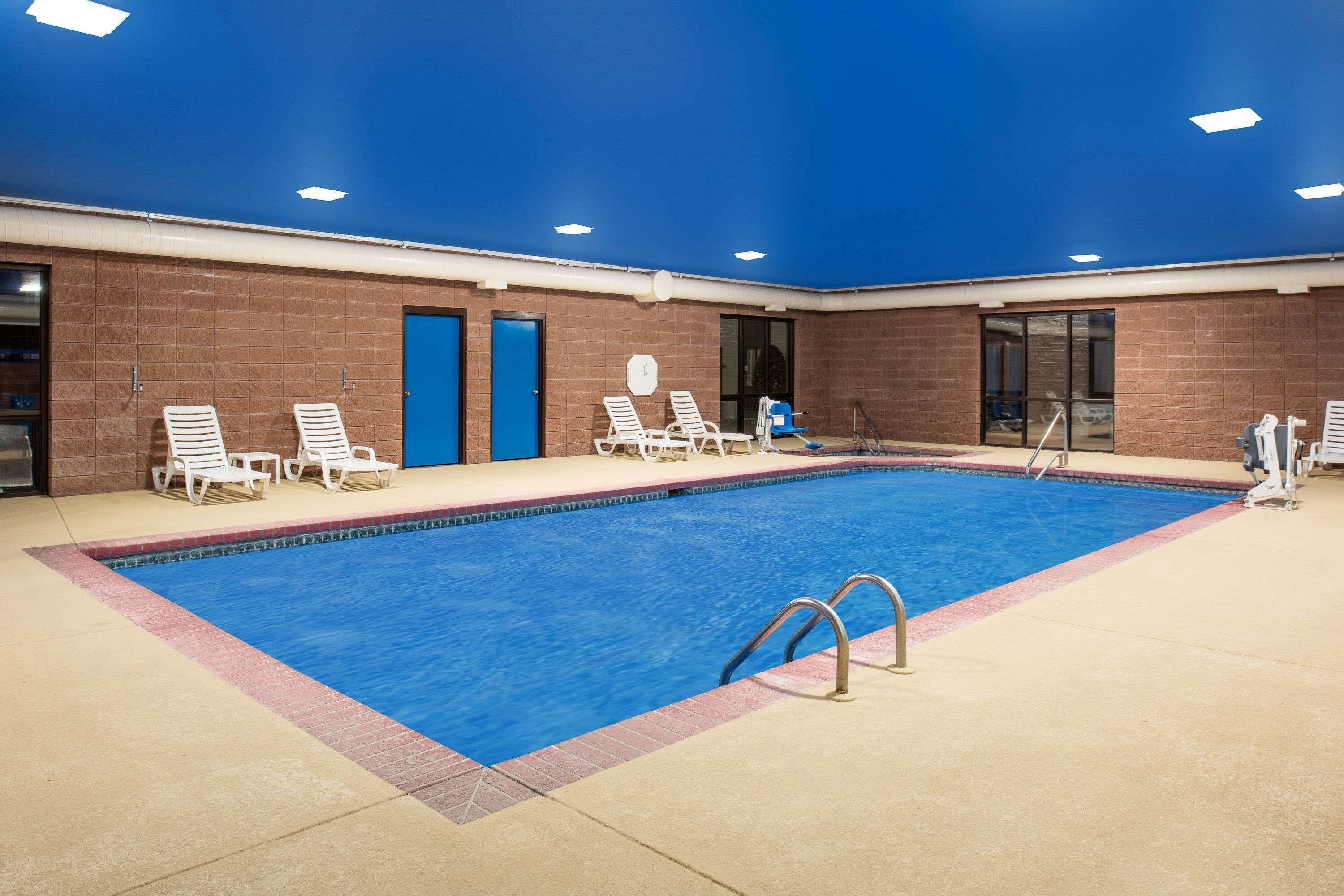 Une piscine intérieure à l’eau d’un bleu cristallin, entourée de chaises longues blanches et dotée d’un sol carrelé.