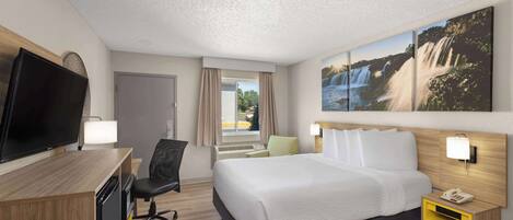 A hotel room with a bed, a desk with a TV, a chair, a nightstand with a phone, and a window with curtains.