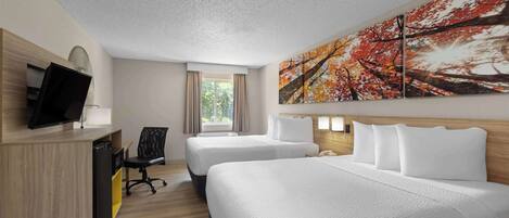Habitación de hotel con dos camas, un escritorio, una silla, un televisor y un cuadro grande con motivos otoñales.