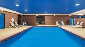 A swimming pool with clear blue water, surrounded by white lounge chairs and a brick wall.